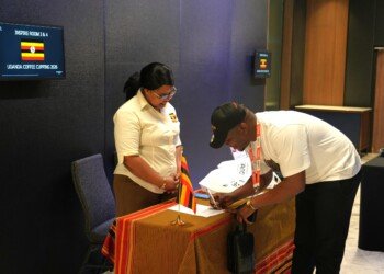 A guest signing in at the Uganda Coffee Cupping 2026 registration desk beside a Uganda flag
