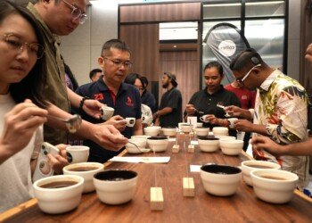 Participants leaning over the cupping table to taste Ugandan coffee from spoons and cups
